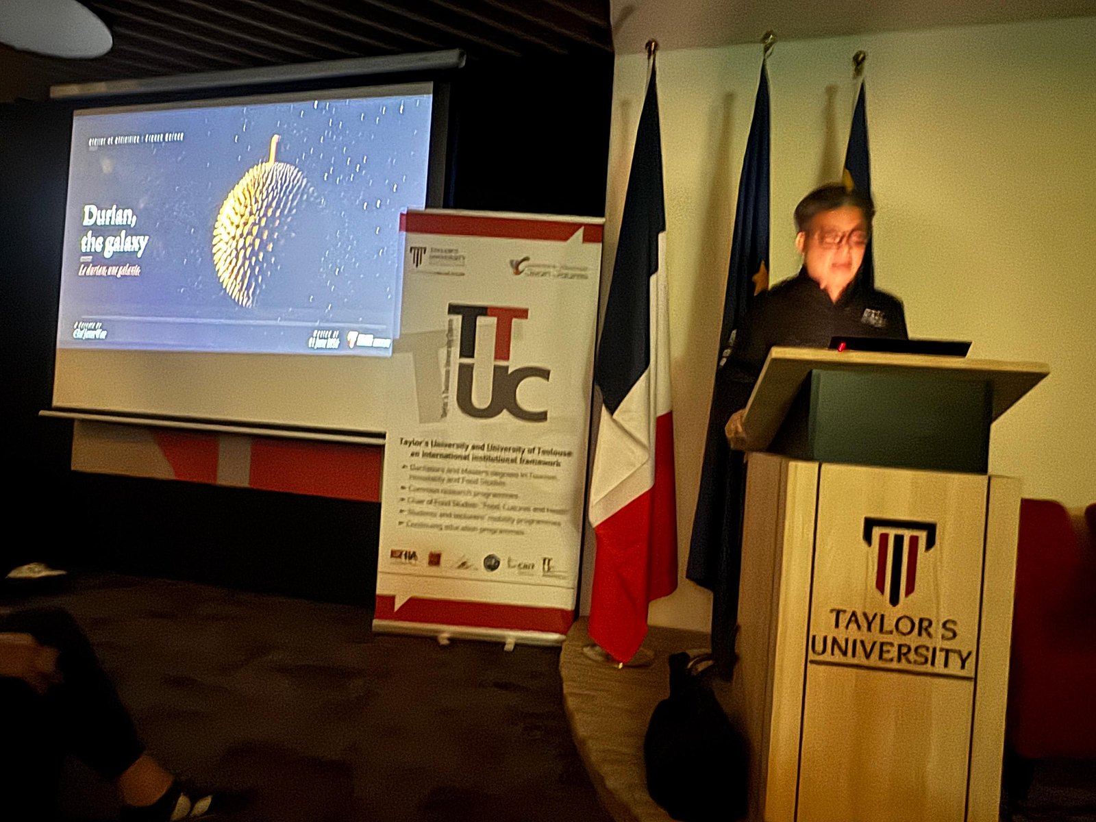 Chef James Won giving the durian keynote at Taylor's, French and Malaysian flags by the lectern