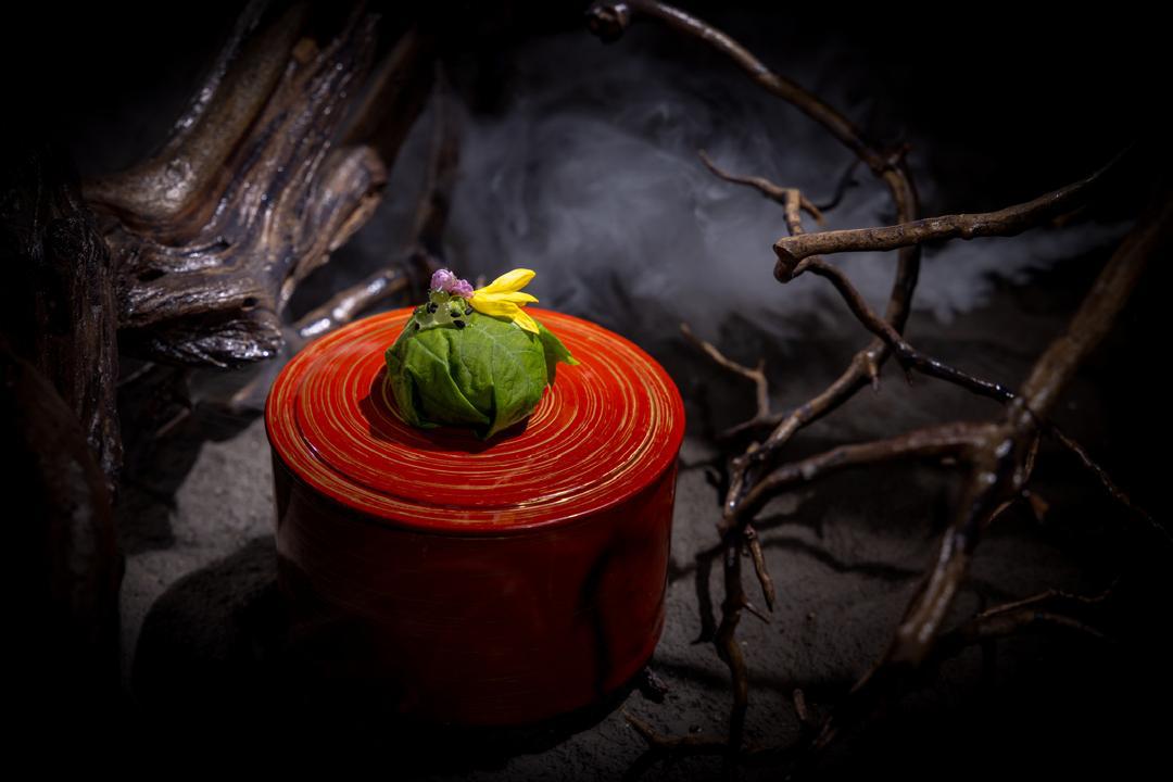 A leaf-wrapped pearl, the third bite of the overture trio, on a red lacquer vessel
